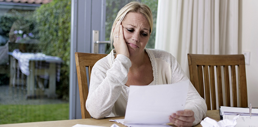 Blonde woman sitting at a table looking concerned while reading a piece of paper