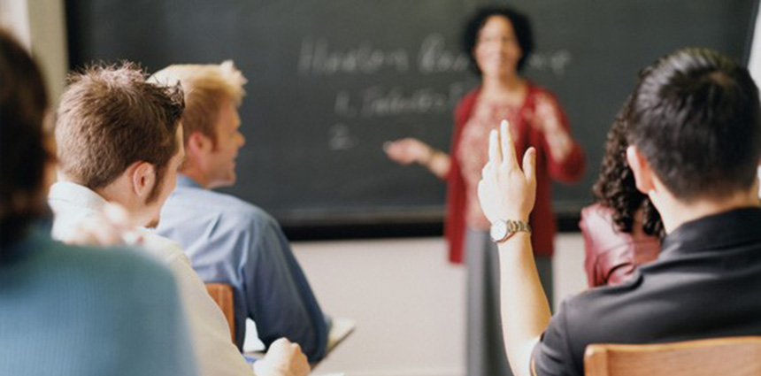 Female teacher in front of a classroom with a young man raising his hand