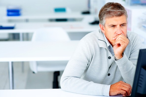 A man sitting in front of a computer monitor with white chairs and tables in the background