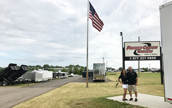 Happy couple standing outside of their small business with an American Flag on a pole