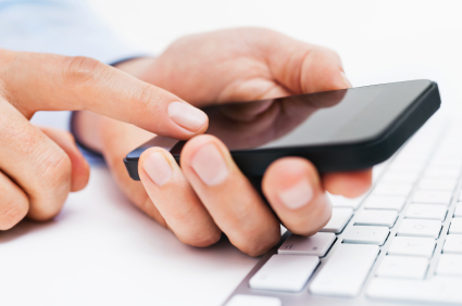 A pair of hands holding a smart phone near a keyboard