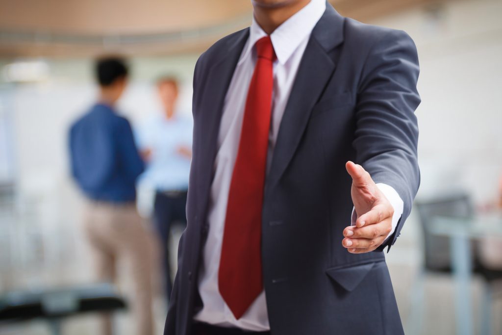 A businessman wearing a blue suit and a red tie offering a hand for a handshake