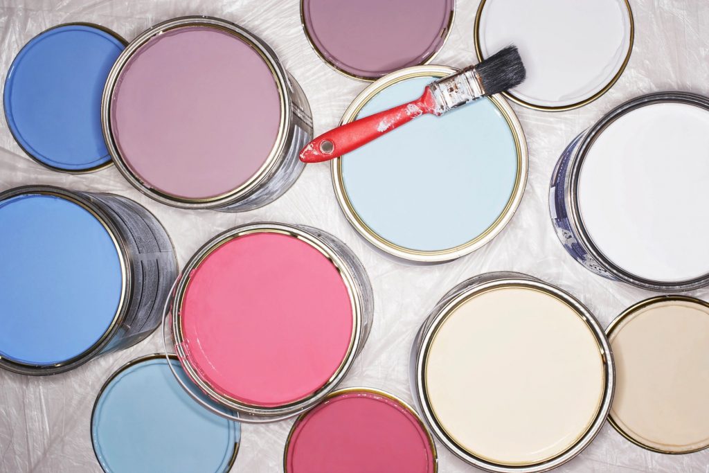 Six open full paint cans with lids and a paint brush resting atop one of the cans