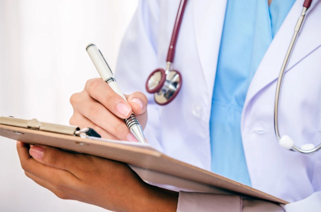 Close-up of a doctor writing on a clipboard