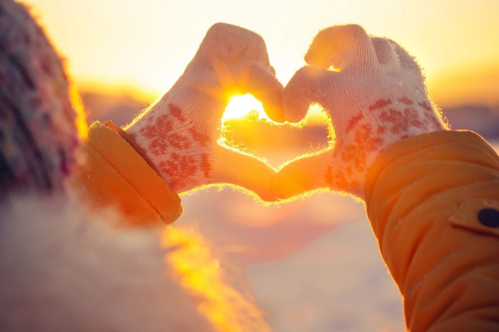 A person making a heart shape with their hands during a sunset