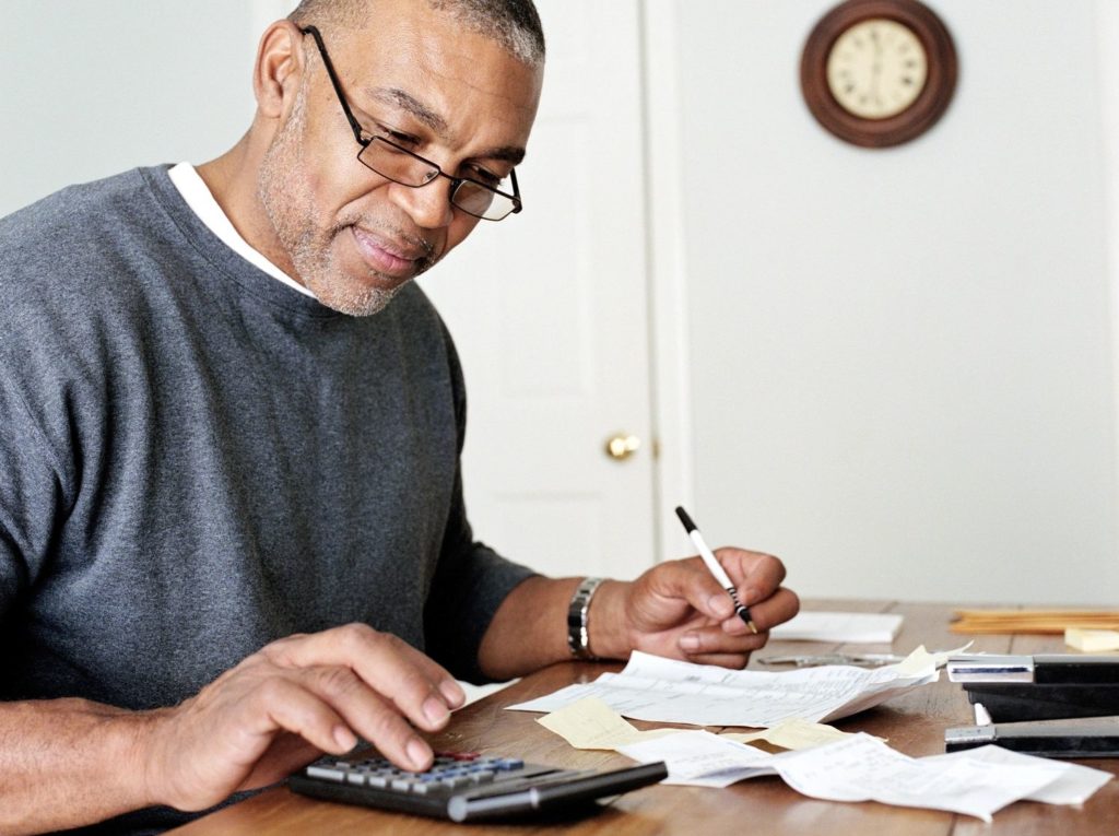 An older gentleman wearing a grey sweatshirt balancing his checkbook at a dinner table