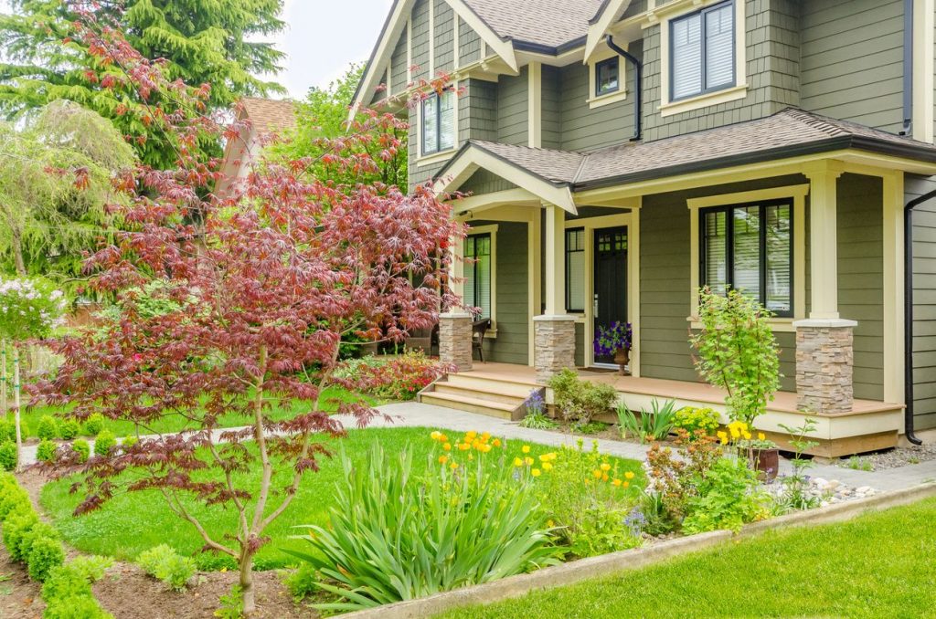 An olive green house with a well-manicured lawn and flowerbeds