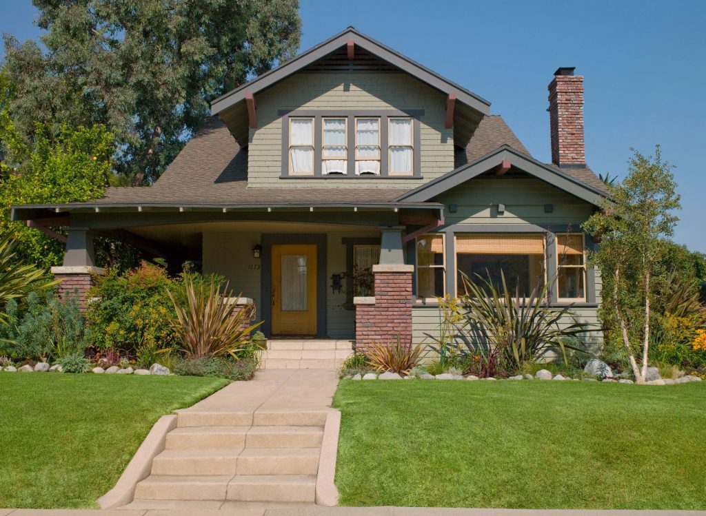 An olive green bungalow with a yellow door on a sunny day