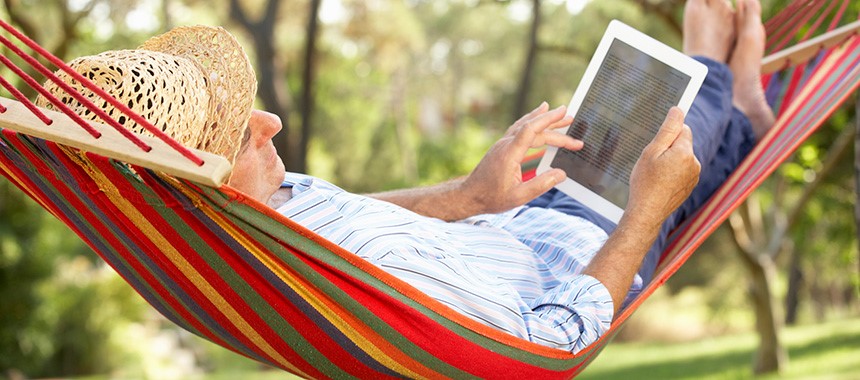 A man with a sun hat laying on a colorful stripe hammock while using a tablet