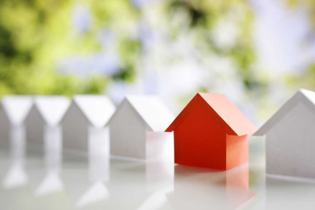 A row of white model houses of white with one red one in front of a tree-filled landscape