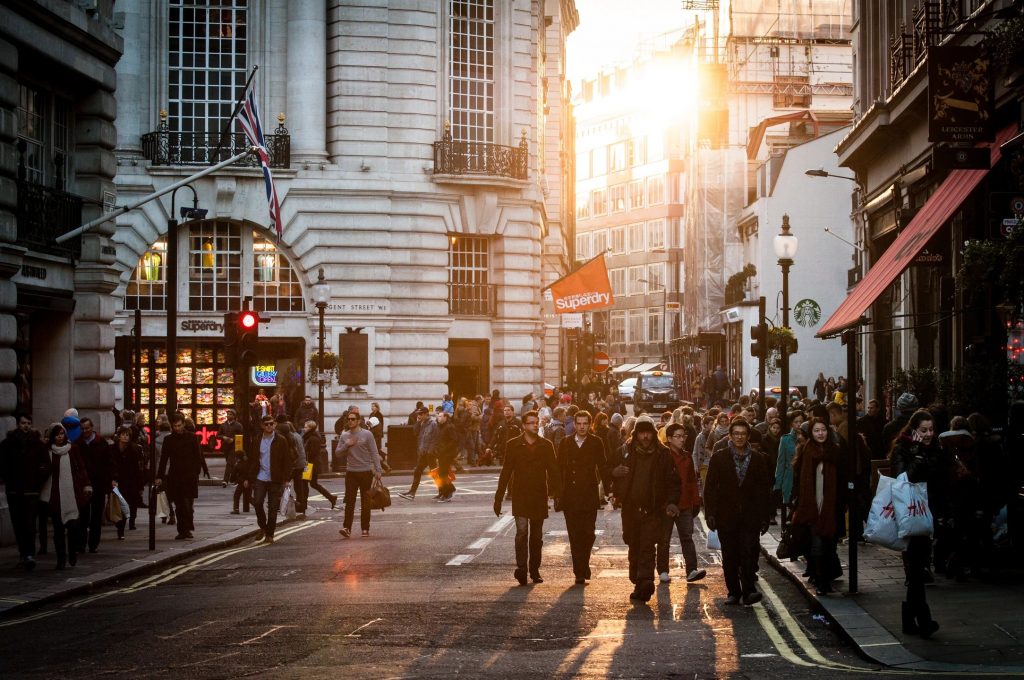 A crowded downtown area with many pedestrians and light filtering through tall buildings