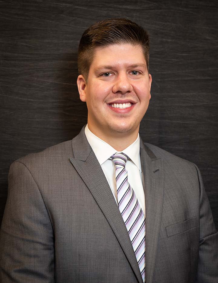 A young man smiling in a grey suit with a striped tie