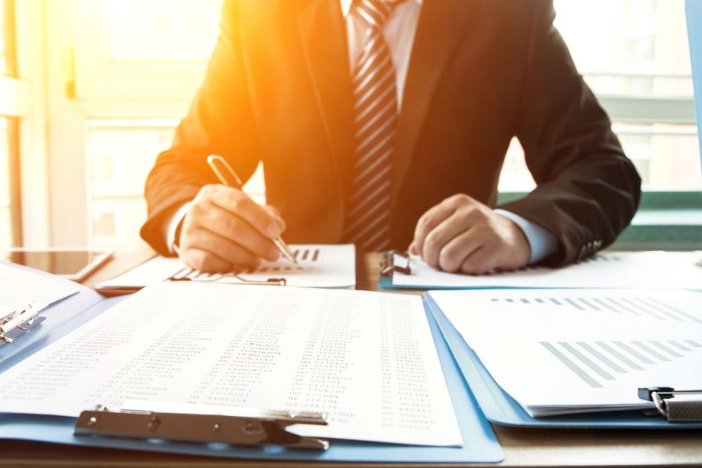 A man writing notes on bar graphs spread out on his desk with the sunlight poking through over his shoulder