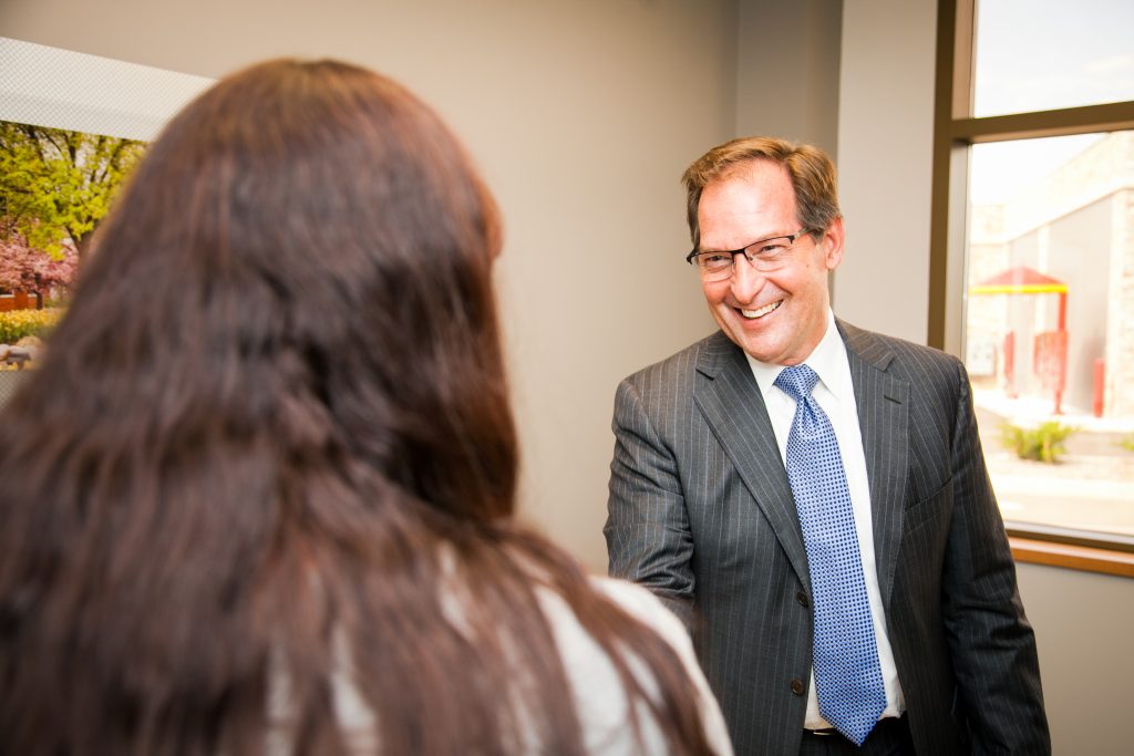 A man in a pin-striped suit and blue tie smiling at a woman in an office