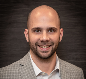 A man with a very short beard with a grey plaid sport coat smiling