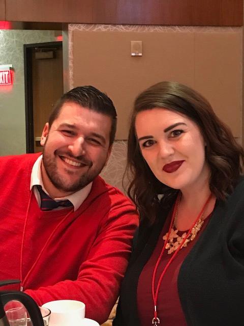 A man and woman sitting at a dinner table wearing red and smiling