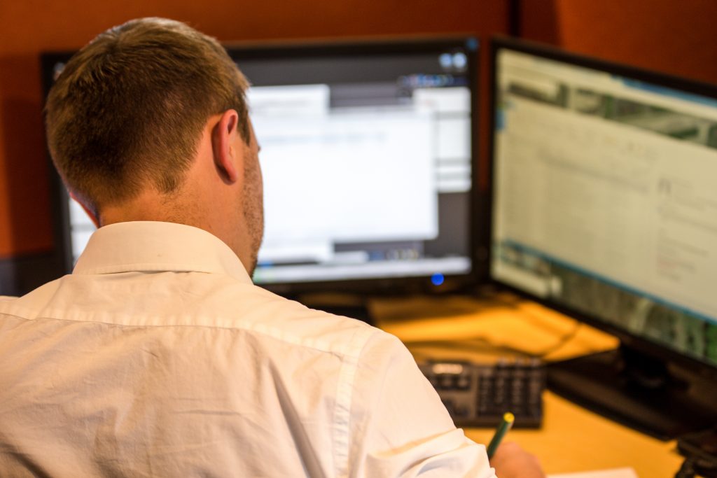 Rear view of a man sitting at a desk in front of two computer screens