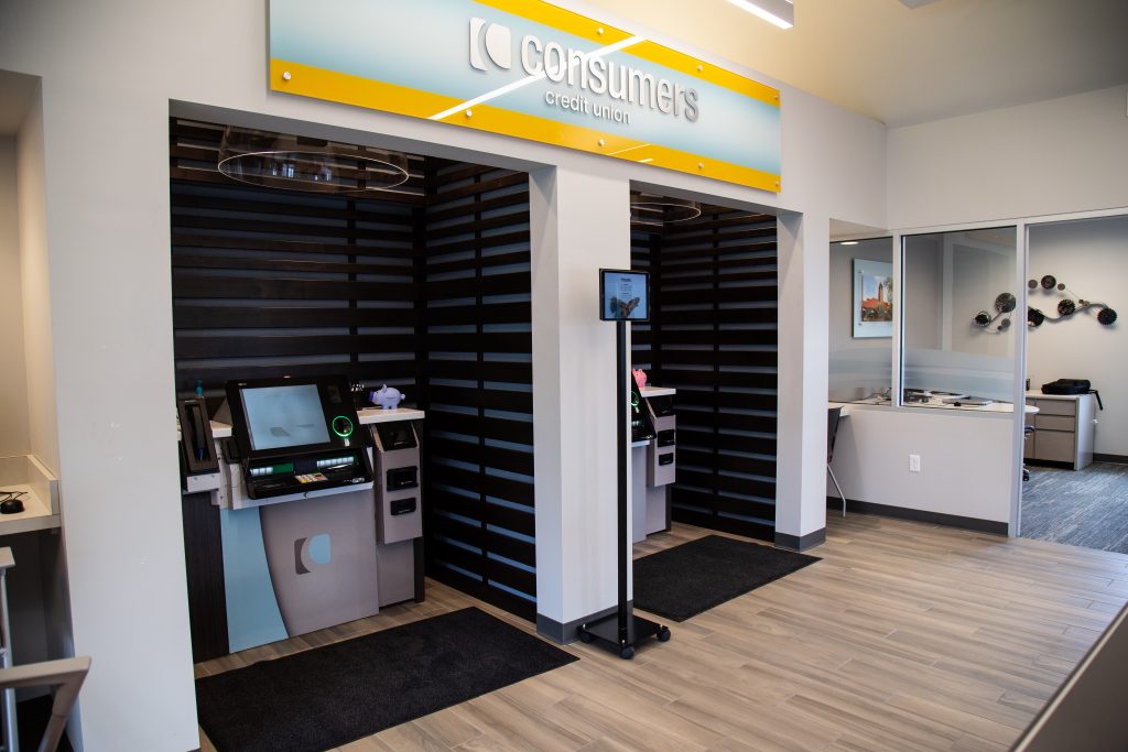 An angled side view of two ATM kiosks underneath a yellow Consumers Credit Union sign