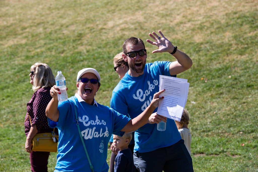 Two people smiling and waving to the camera while at a fundraising walk event