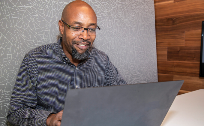 A man on a laptop in front of a grey background wall