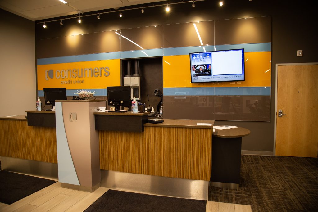 A brown wall with an orange Consumers Credit Union sign behind bank teller windows