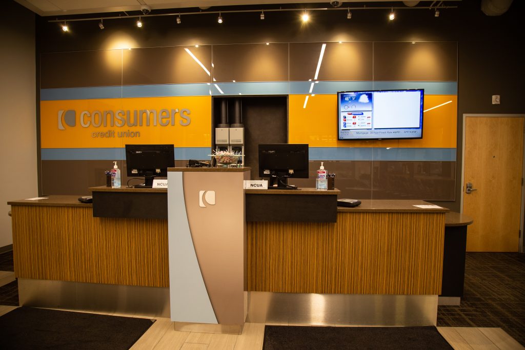 A Consumers Credit Union office with an orange Consumers sign behind two teller desks