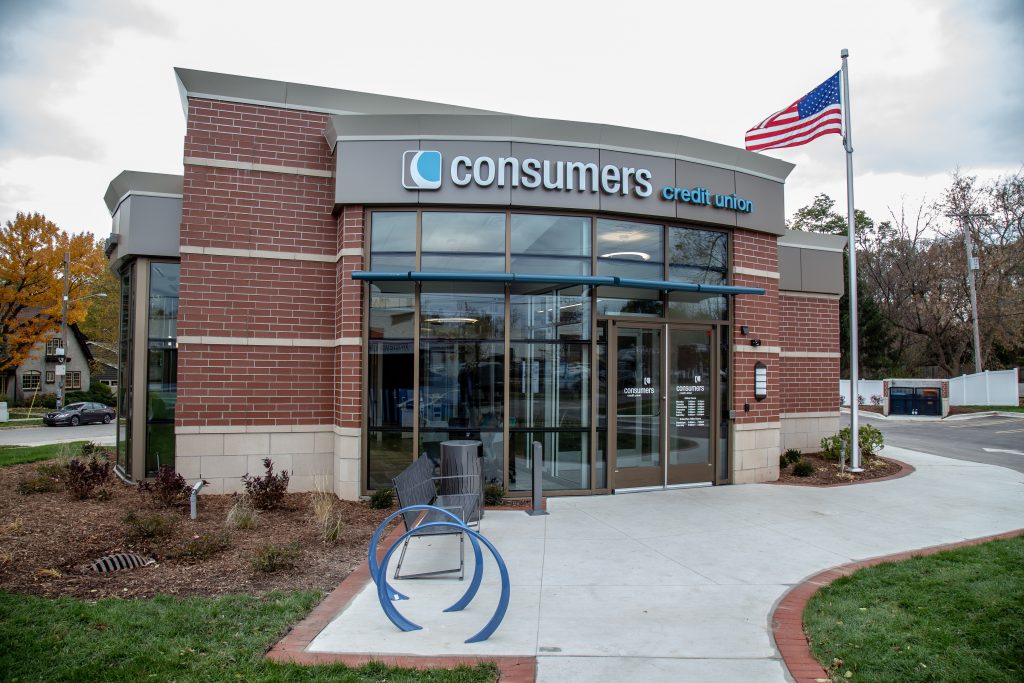 A Consumers Credit Union office with an American flag and a bench out front