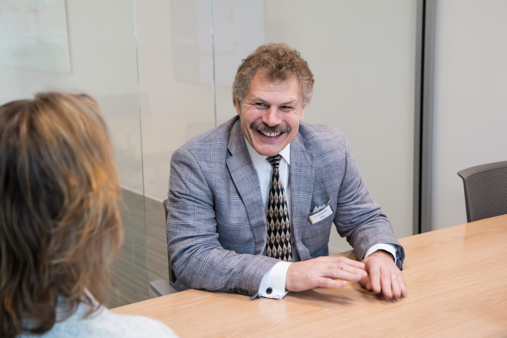 A man with a mustache and a grey plaid suit smiling at a table