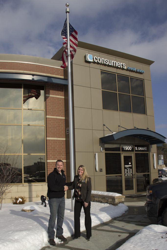 A young man and woman shaking hands outside of a Consumers Credit Union office on a snowy day