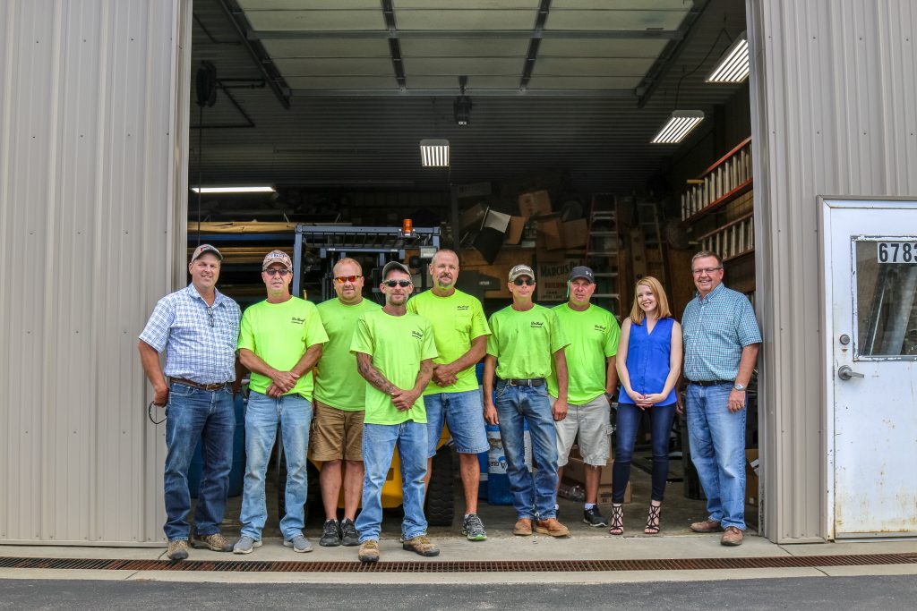 A large group posing for a picture while standing in a large bay door of a warehouse