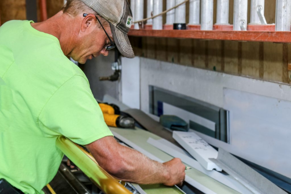 A man wearing a bright green shirt measuring building material at a workbench