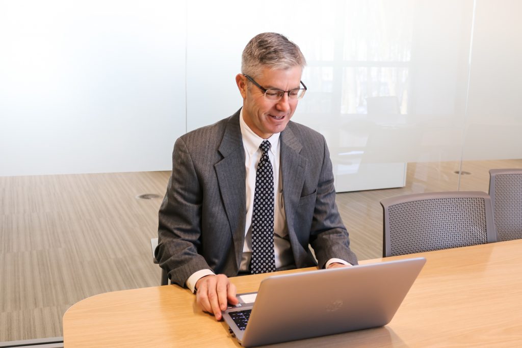 A gentleman with grey suit working on a laptop sitting at a conference table