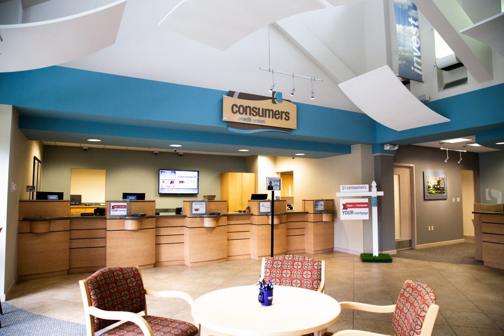 A round table with three chairs in front of four Consumers Credit Union teller windows