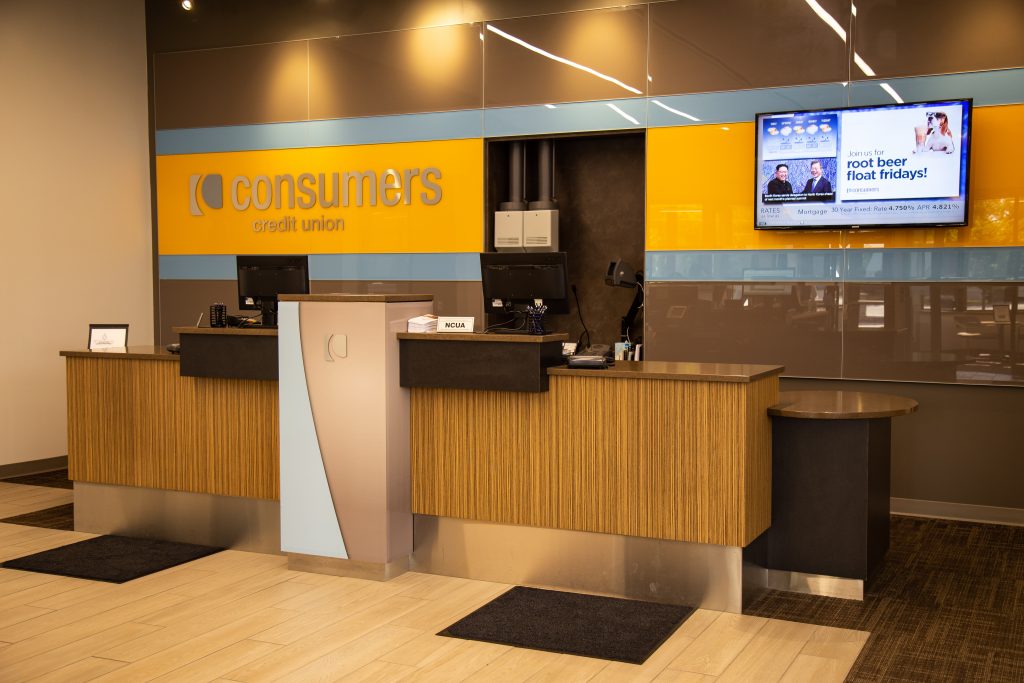 Two teller windows in front of an orange Consumers Credit Union sign