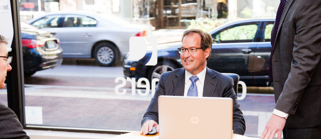 Three men speaking to each other around a conference table in front of a large window with the Consumers Credit Union logo