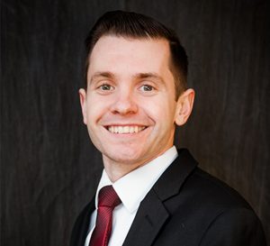 Man wearing a red tie and a black suit smiling