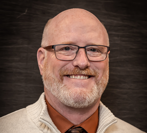 A man with a beard and glasses wearing an orange shirt