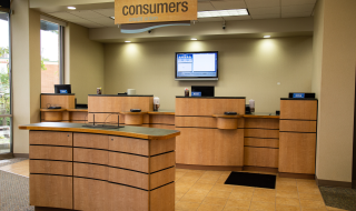 A Consumers Credit Union office with teller service counter in the background and a standing height kiosk for withdrawal and deposit slips in the foreground