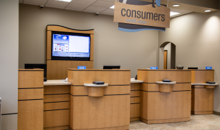 A Consumers Credit Union branch with three teller stations and a TV screen behind them