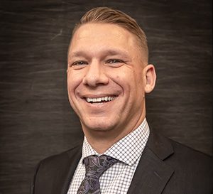 A man with short blonde hair smiling for a photo wearing a coat and tie