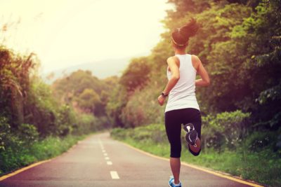 A woman with a ponytail and white tank top running down a country road