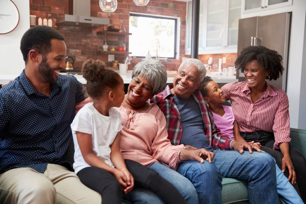 A pair of grandparents with their grandkids and the children's parents on a couch smiling