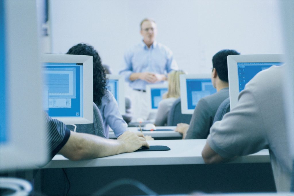 An instructor speaking at the front of a computer lab