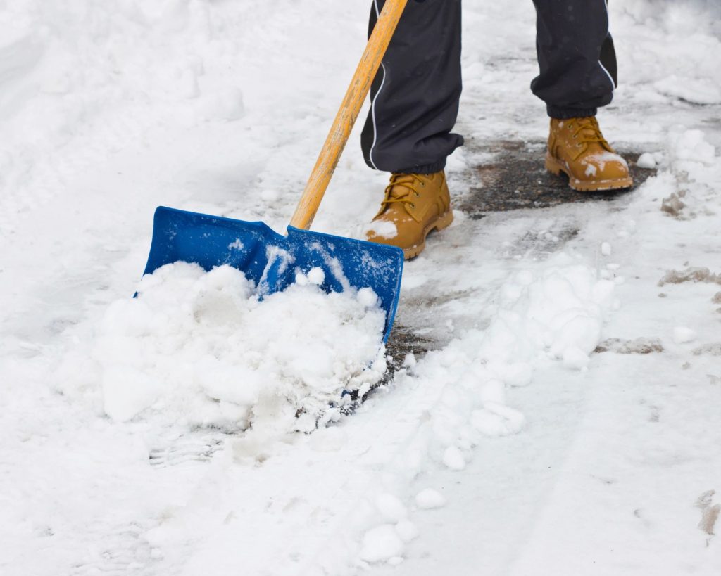 A close-up of someone wearing work boots shoveling snow