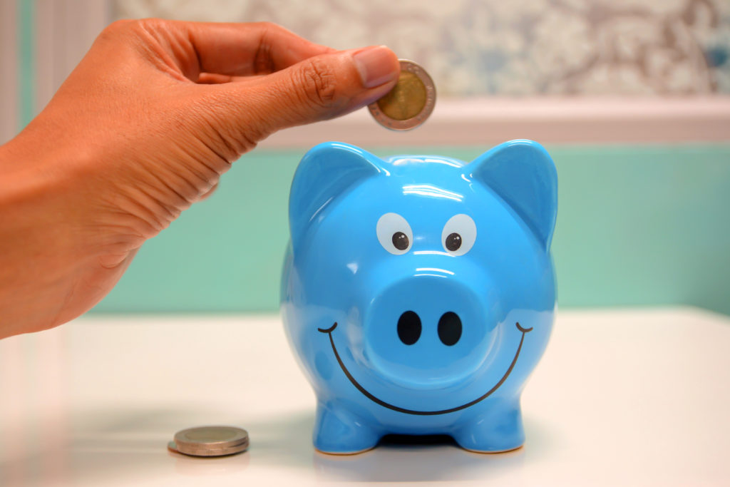 Hand putting coin into smiling blue piggybank