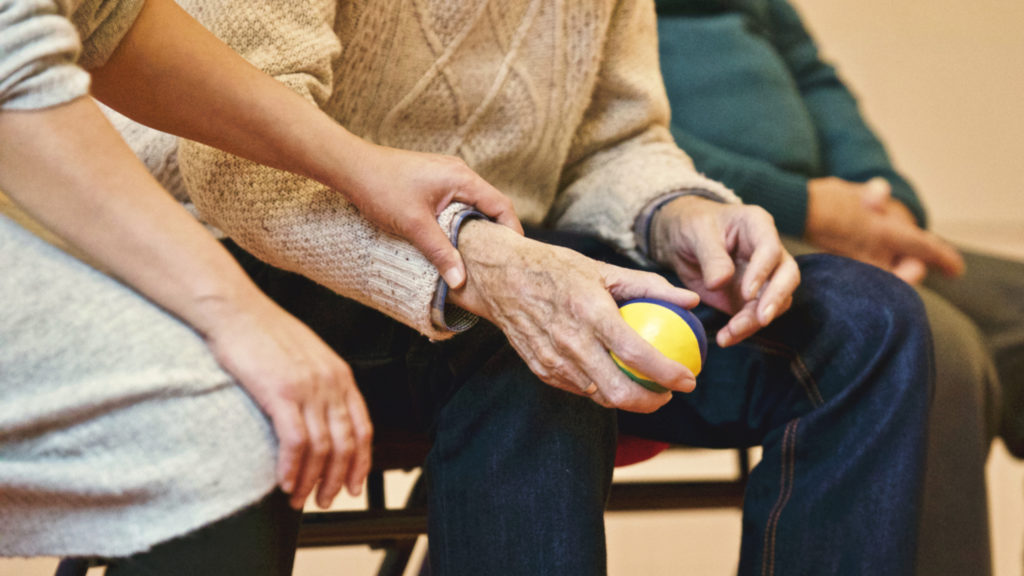 Young adult person sitting next to and holding the arm of an elderly man