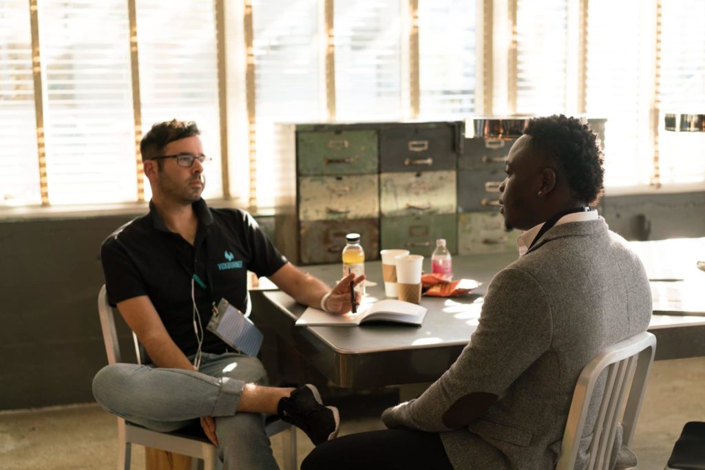 Two men sit across a table from each other talking in an office