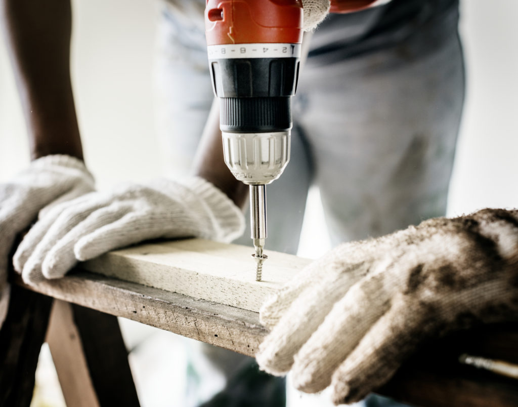 Repairman wearing white gloves drilling screw into wood plank