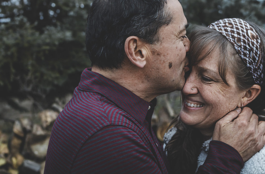 Mature couple embraces as husband kisses his smiling wife on her forehead