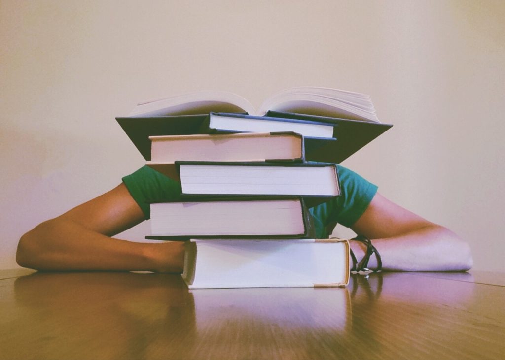 a man has hid head on a desk behind a pile of books